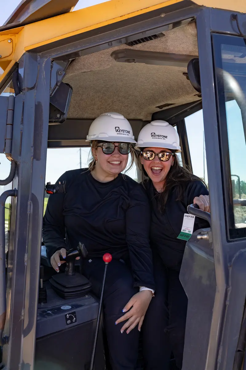 Two staff members in an excavator cab at the groundbreaking
